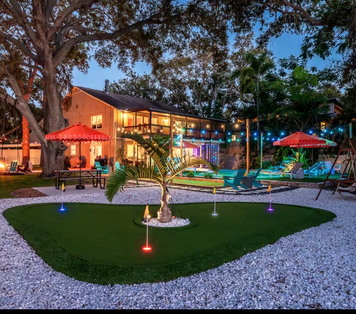 Backyard putting green and patio lit by low-voltage landscape lighting at dusk