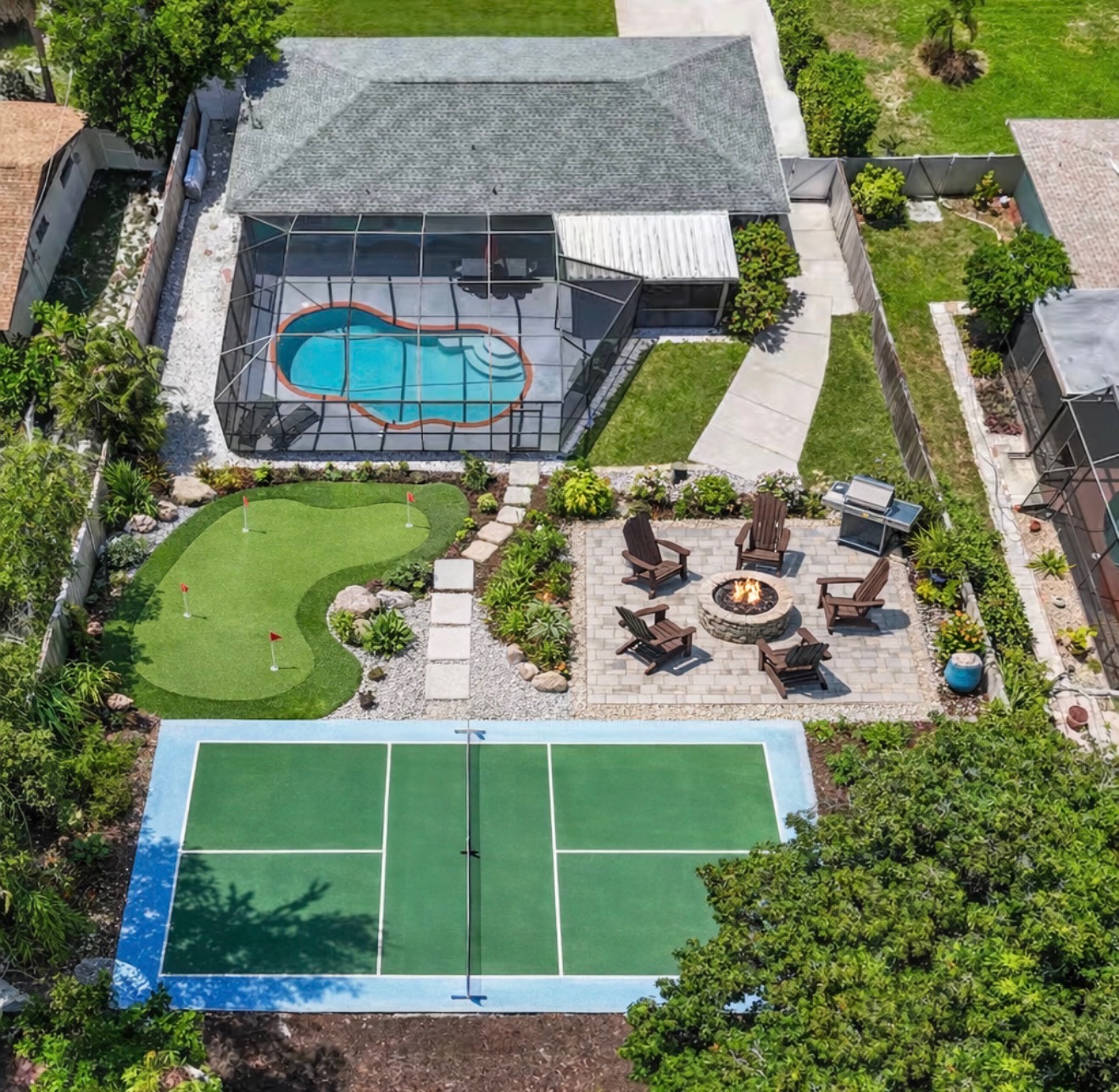 Aerial view of a Mocte-built backyard with screened pool, artificial putting green, paver fire-pit patio and pickleball court